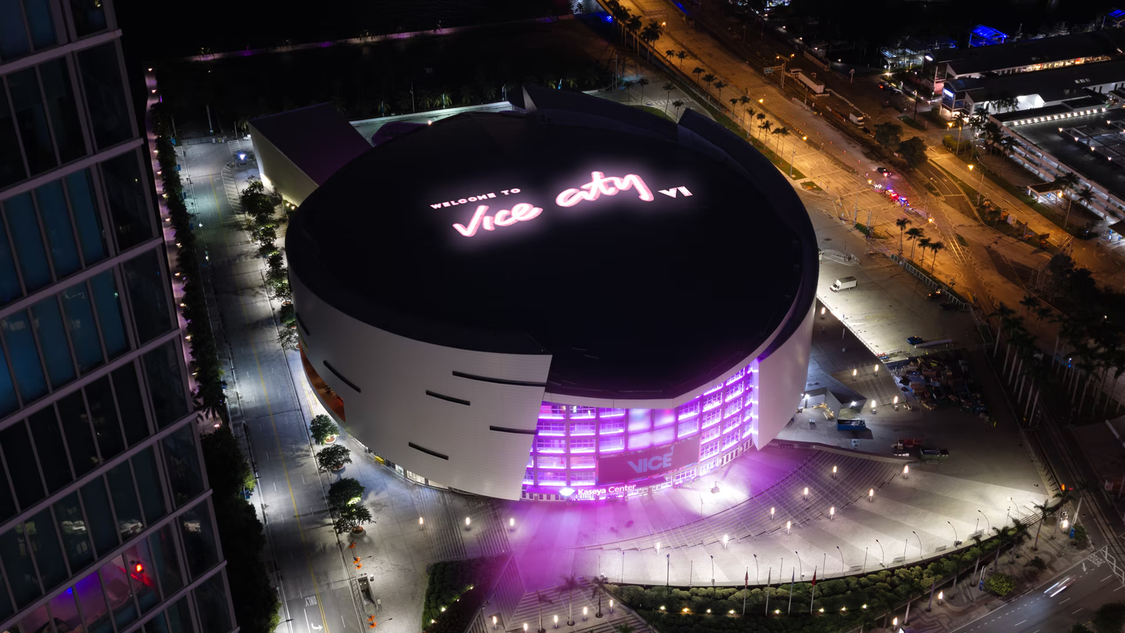 Aerial night view of the Kaseya Center in Miami with 'Welcome to Vice City VI' lit up on its roof and the arena glowing pink