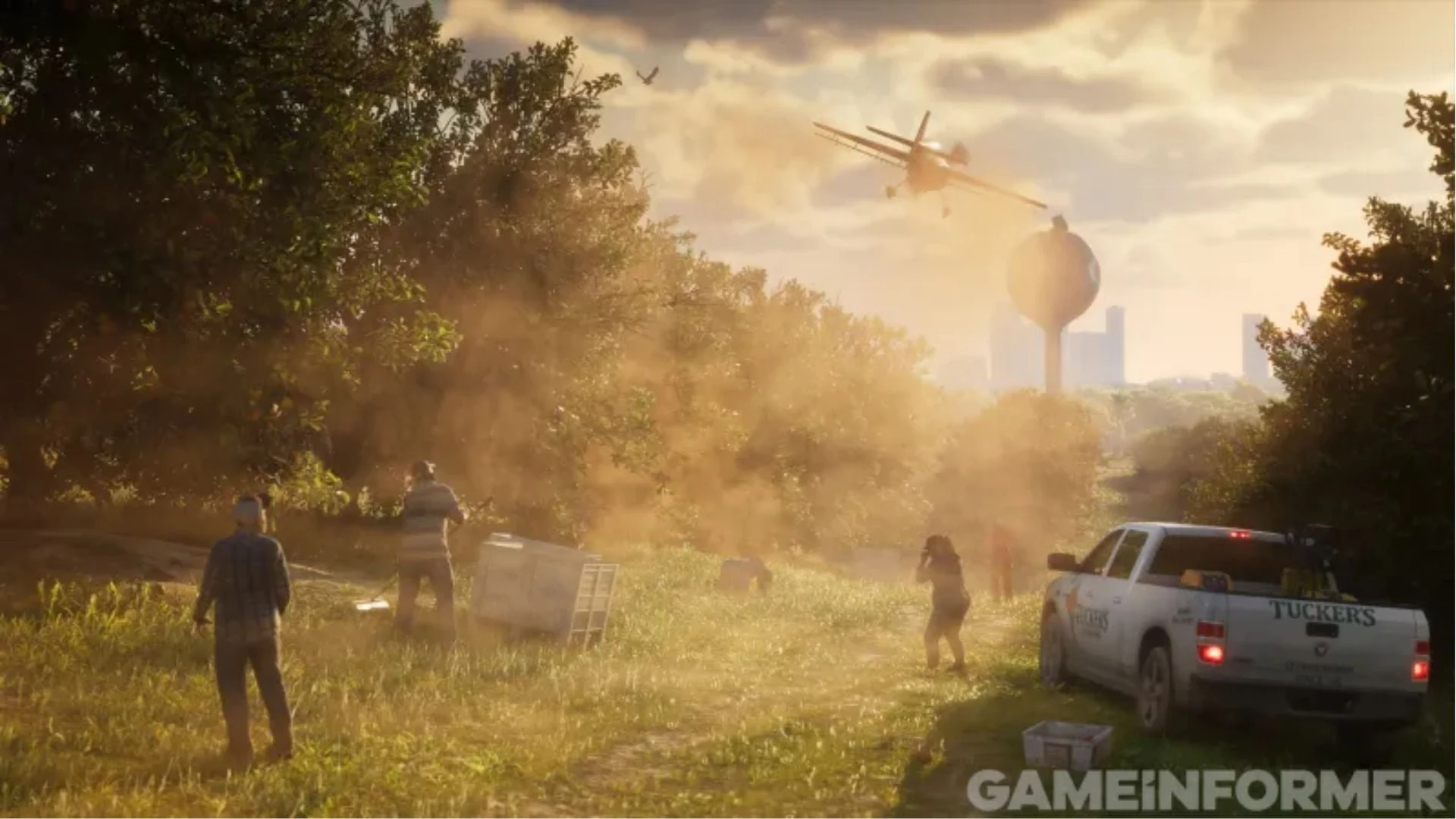 A crop duster sprays low over a field next to a water tower and a Tucker's pickup truck